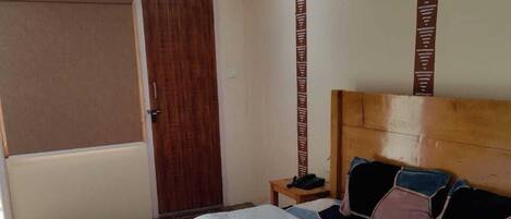 A bedroom with a wooden ceiling, a bed with a grey bedspread, a wooden headboard, a bedside table with a phone, and a door with a brown pattern.