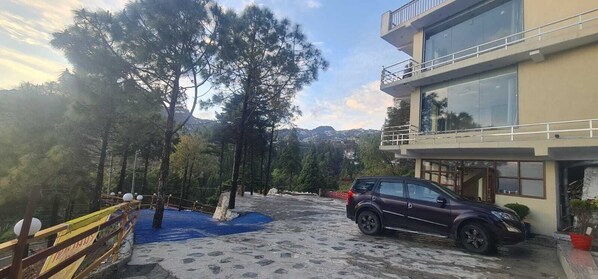 Ένα σύγχρονο κτίριο με μεγάλα παράθυρα, χώρο στάθμευσης και μια δασώδη περιοχή που περιβάλλεται από ξύλινο φράχτη.
