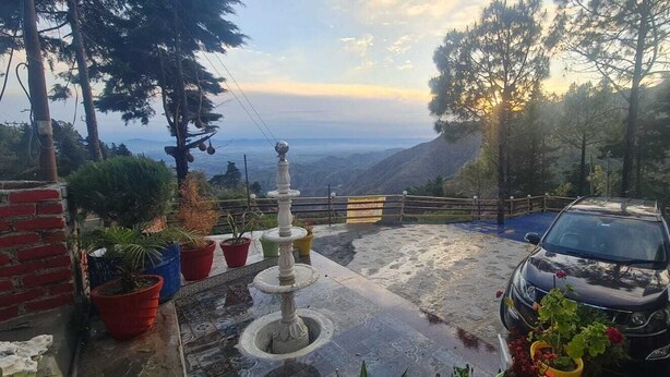 A paved area with a fountain, potted plants, and a parked car. - Rudraksh Resort (Mussoorie)