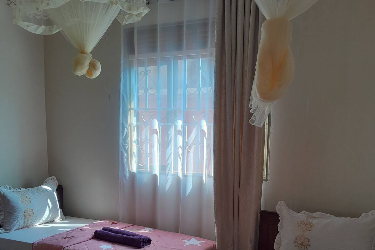 A bedroom with two beds, a window with curtains, and a hanging mosquito net.