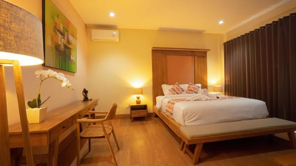 A hotel room with a wooden bed, bedside tables, a desk, a chair, and a potted plant.