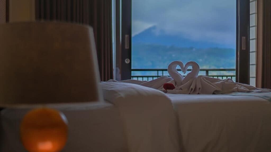 Ett hotellrum med en säng, utsikt över bergen och en hjärtformad dekoration på sängen.
