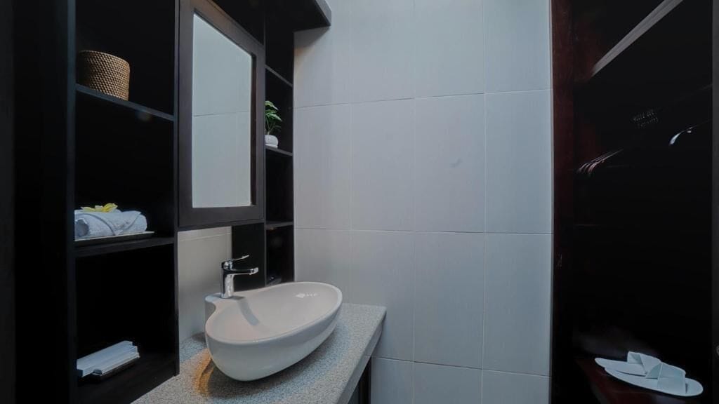 A modern bathroom with a white sink, dark shelving, and a mirror.