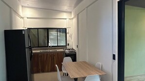 Una cucina compatta con frigorifero, fornello e finestra. In primo piano, un tavolo da pranzo con sedie.