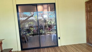Un terrazzo in legno con una porta scorrevole in vetro che dà su uno spazio esterno con vista sugli alberi e un patio.