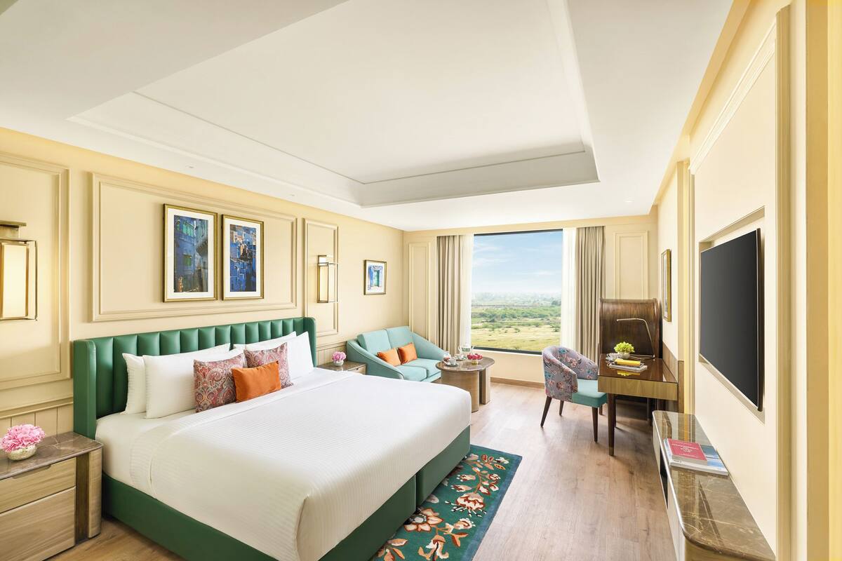 A hotel room with a large bed, a desk with a chair, a small table, and a television.
