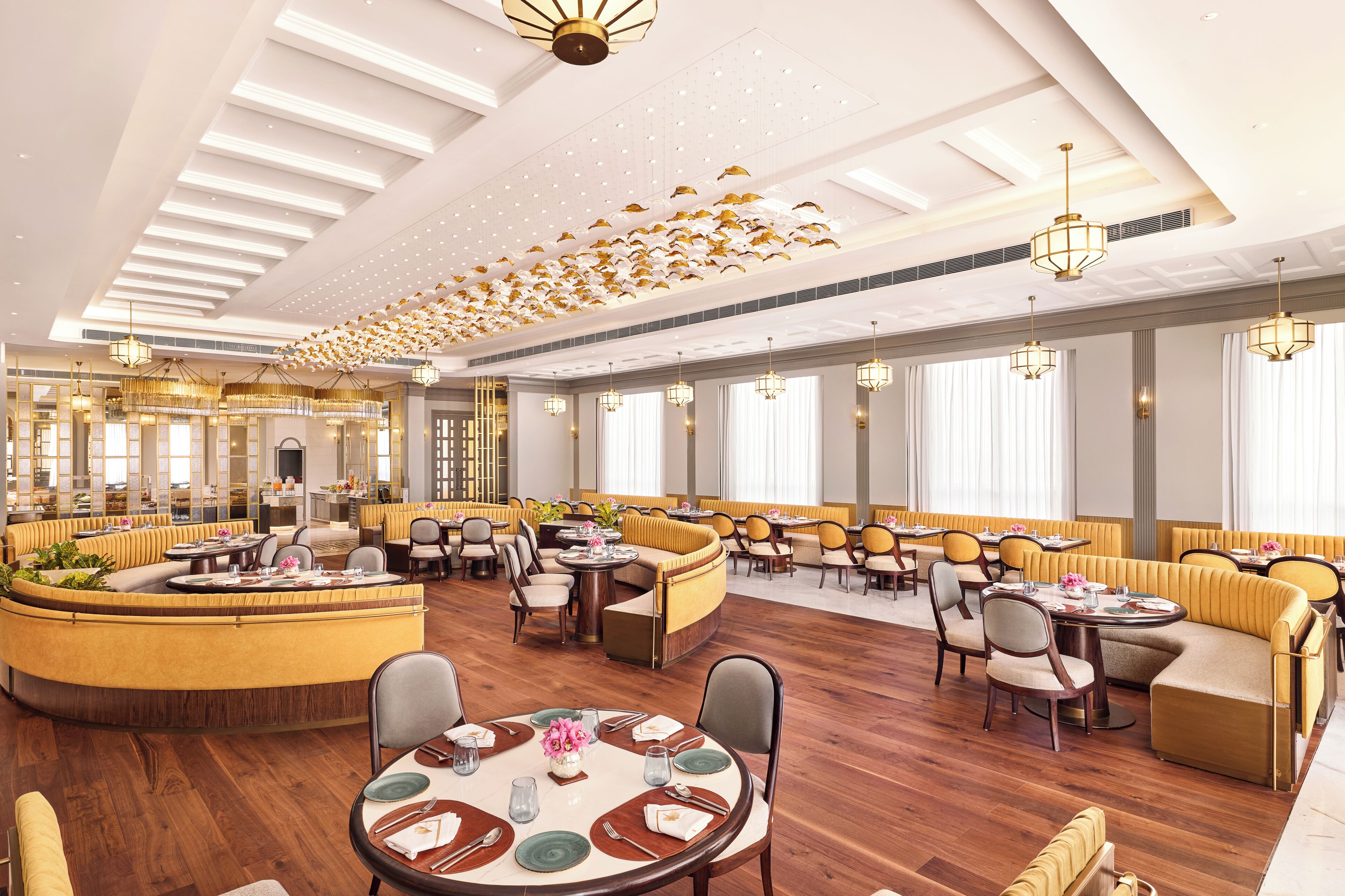 A spacious dining area with high ceilings, chandeliers, and a variety of seating arrangements including round tables and cushioned booths.