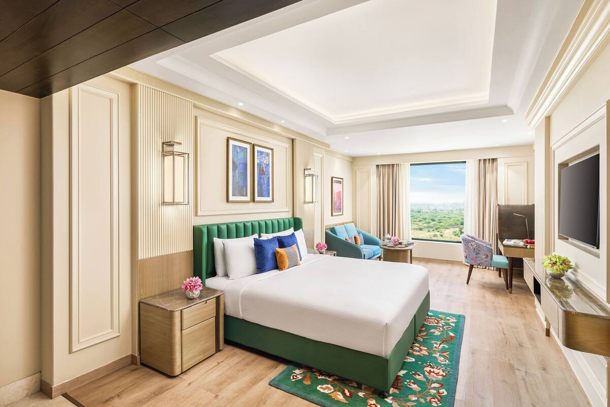 A hotel room with a large bed, a desk, a TV, and a view of the outdoors.
