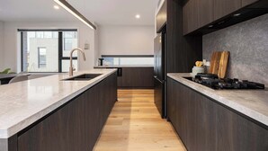 A modern kitchen with dark wood cabinets, a large island with a sink, and a gas stove. - Rooftop Deck & Sauna, 350m to Safety Beach (Safety Beach)