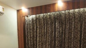 Une chambre d’hôtel avec un lit, une tête de lit en bois, un rideau à motifs et un plaid rouge.