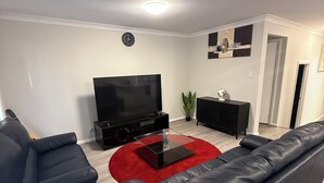 A modern living room with a flat-screen TV, black leather sofas, a red rug, and a minimalist decor.