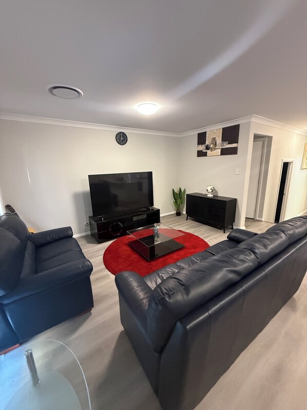Un salon moderne avec un téléviseur à écran plat, des canapés en cuir noir, un tapis rouge et une décoration minimaliste.