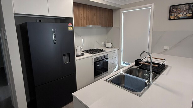 A modern kitchen with a black refrigerator, white cabinets, a stainless steel sink, and a wooden upper cabinet.