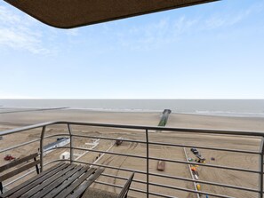 A beach view from a balcony with a metal railing, sandy beach, and a clear sky. - Cosy studio with sea and beach views (Blankenberge)