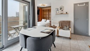A modern apartment with a balcony, a dining area with a table and chairs, a cozy seating area with a chair and cushions, and a wardrobe with shelves. - Nice studio near the beach (Blankenberge)