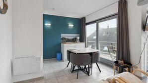 A modern apartment with a dining area, a kitchen, and a large window with a view of buildings. - Nice studio near the beach (Blankenberge)