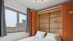 A bedroom with a bed, a window, and built-in wooden shelves. - Nice studio near the beach (Blankenberge)