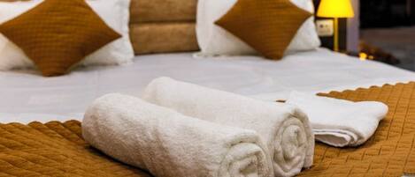 A neatly made bed with white linens and brown pillows, a painting on the wall, and a lamp on the side.