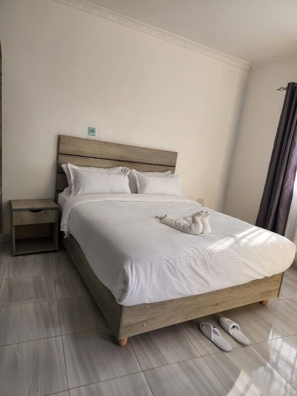 A neatly made bed with white bedding and a wooden headboard, a small bedside table, and a pair of slippers on the floor. - Maara Lodge Chogoria (Chogoria)