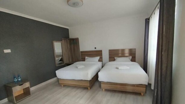 A hotel room with two beds, a small bedside table with a lamp, a mirror, and a window with curtains. - Maara Lodge Chogoria (Chogoria)