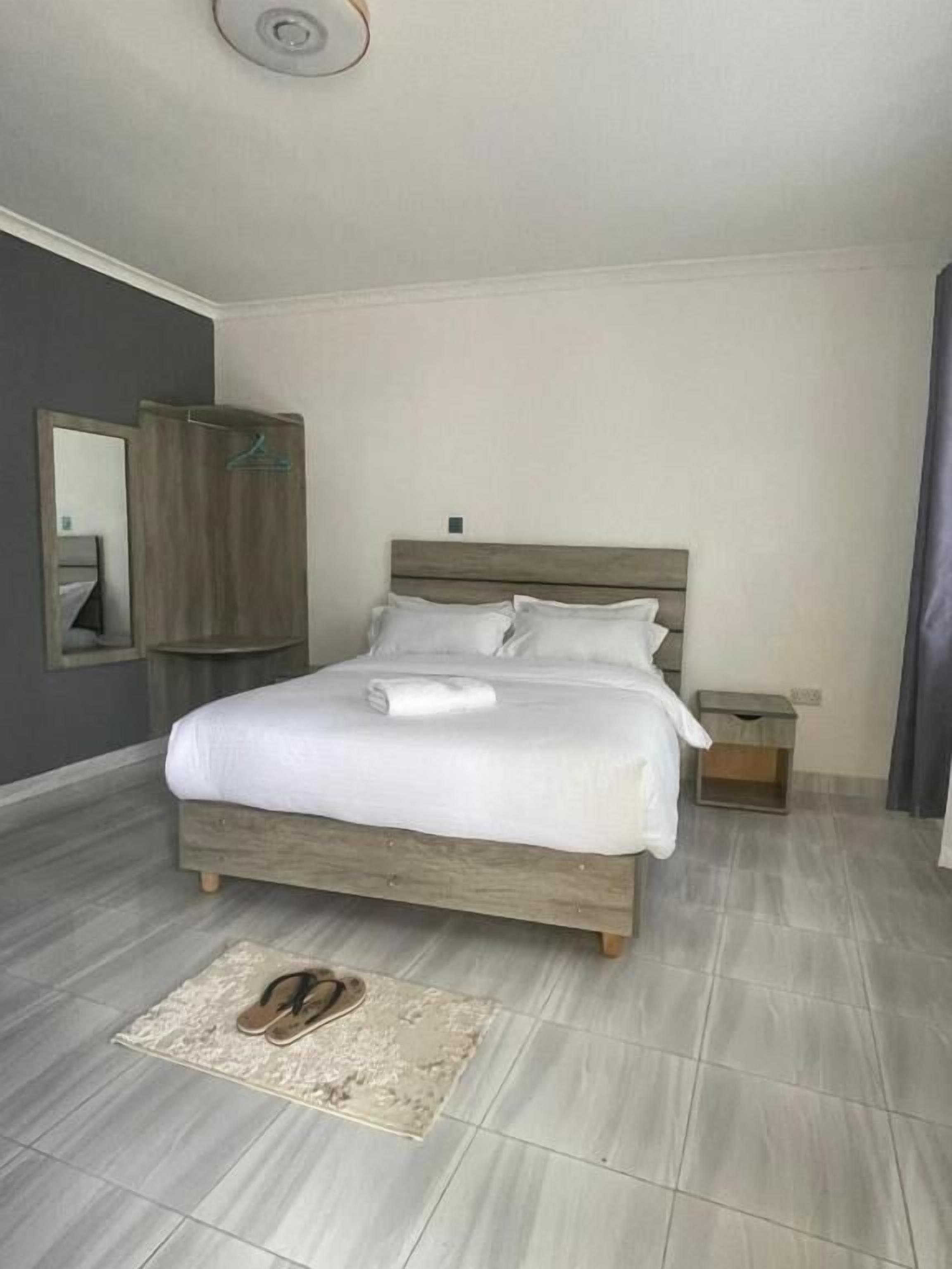 Una cama bien hecha con sábanas blancas, cabecera de madera y una mesita de noche con lámpara.