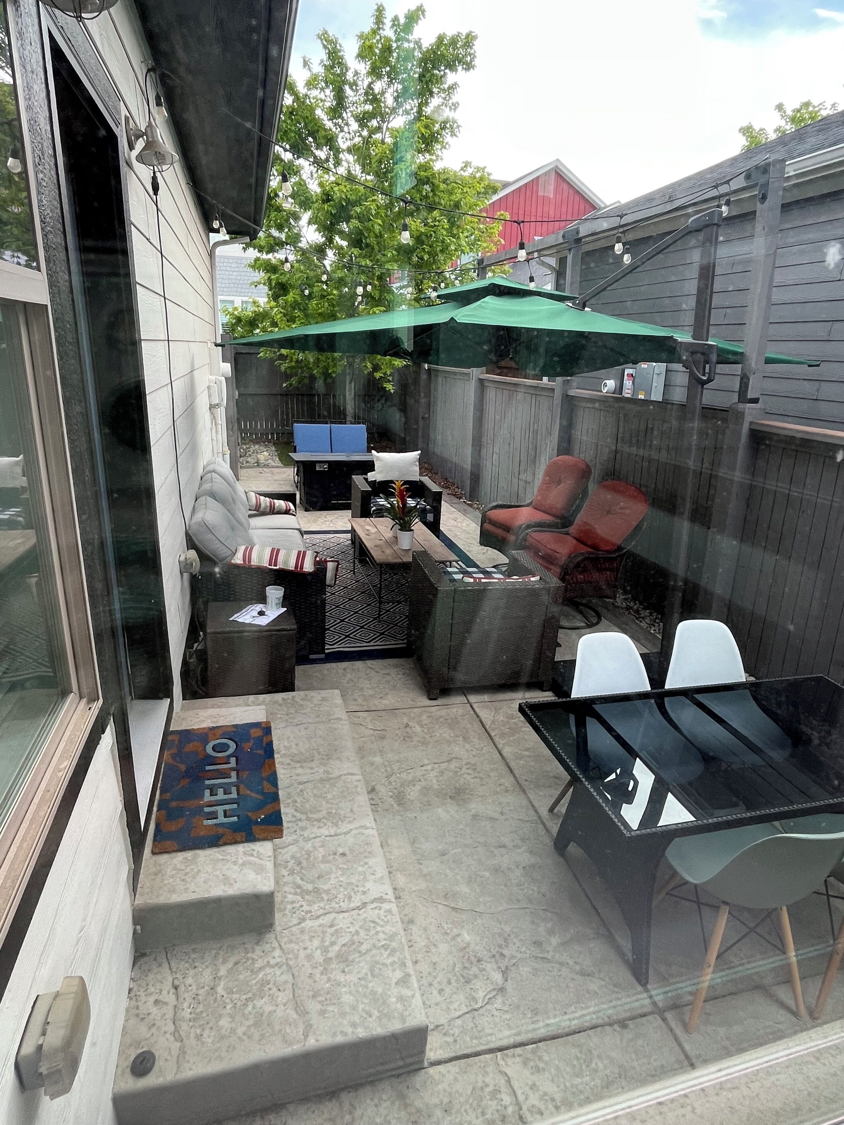 A patio with a glass table, chairs, a fire pit, and a covered seating area.