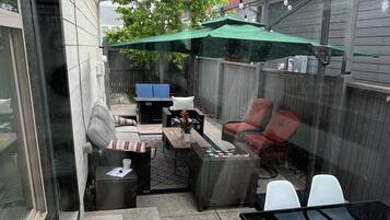 A patio with a glass table, chairs, a fire pit, and a covered seating area.
