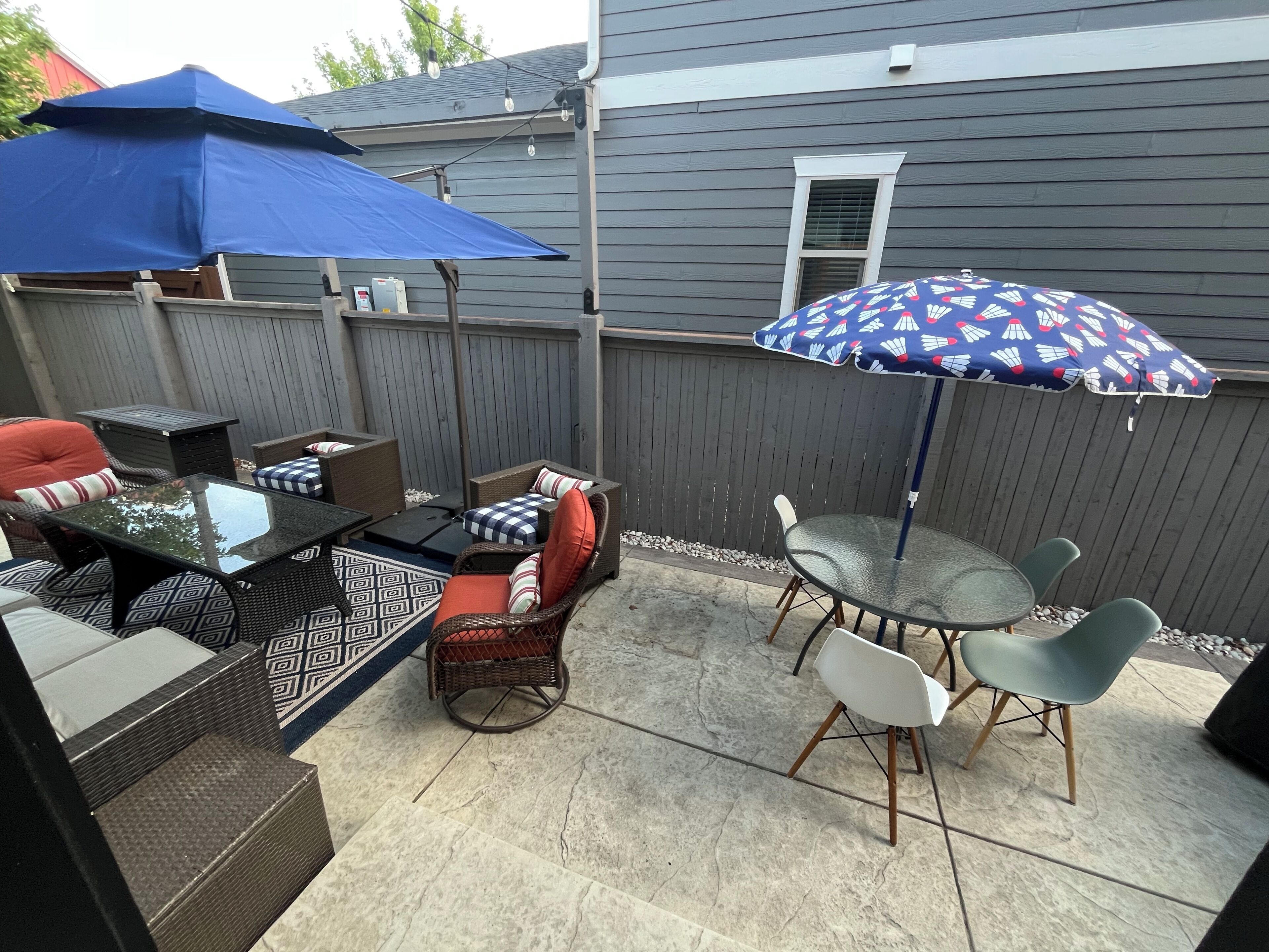 An outdoor patio with a dining table, chairs, and a blue umbrella.