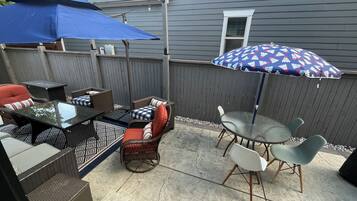 An outdoor patio with a dining table, chairs, and a blue umbrella.