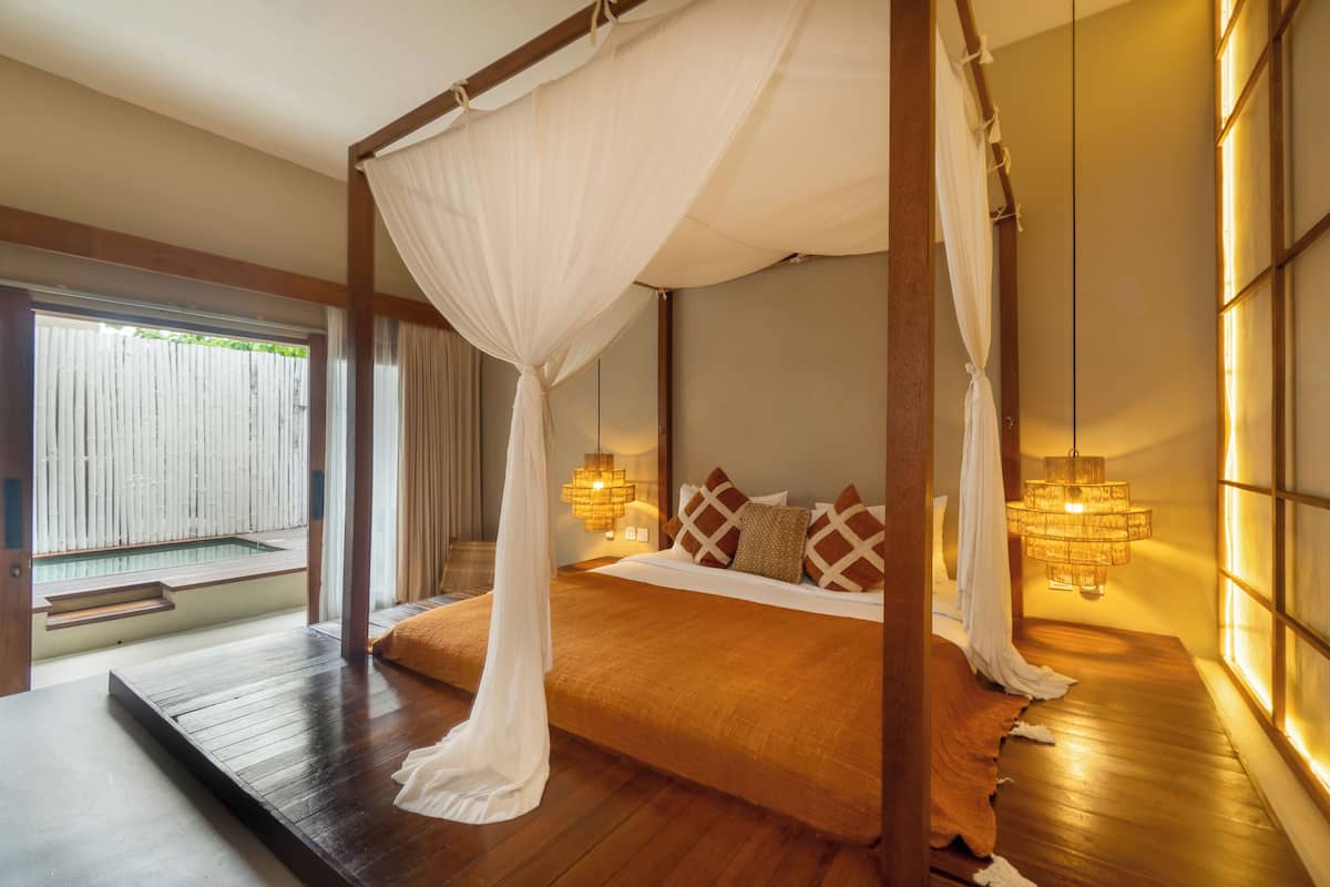 A room with a four-poster bed, wooden flooring, a small pool, and a view of a wooden fence.