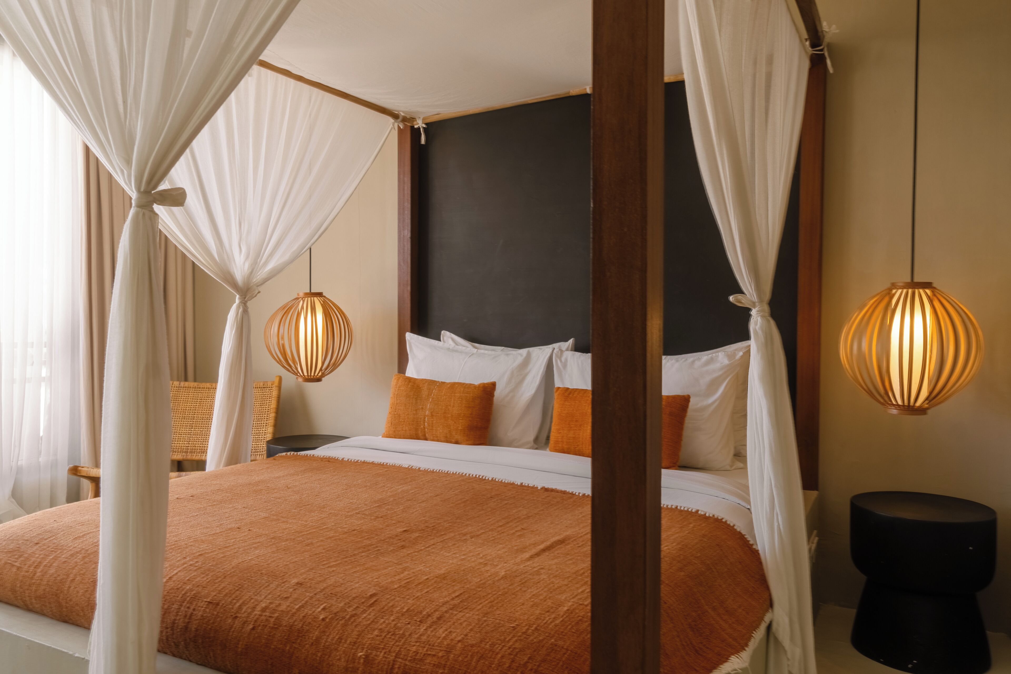 A bedroom with a four-poster bed, white curtains, and two wall-mounted lamps.