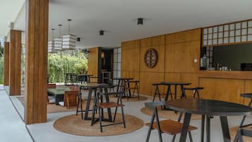 Un espacio exterior moderno para comer con mesas y sillas de madera, una zona de estar central y vistas a zonas verdes.