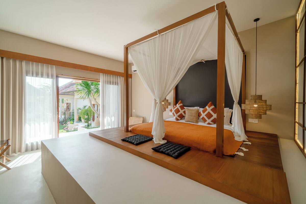 A four-poster canopy bed with a view of a garden and a balcony.