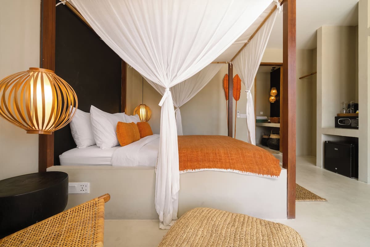 A bedroom with a canopy bed, a wicker chair, a bedside table, and a lamp.