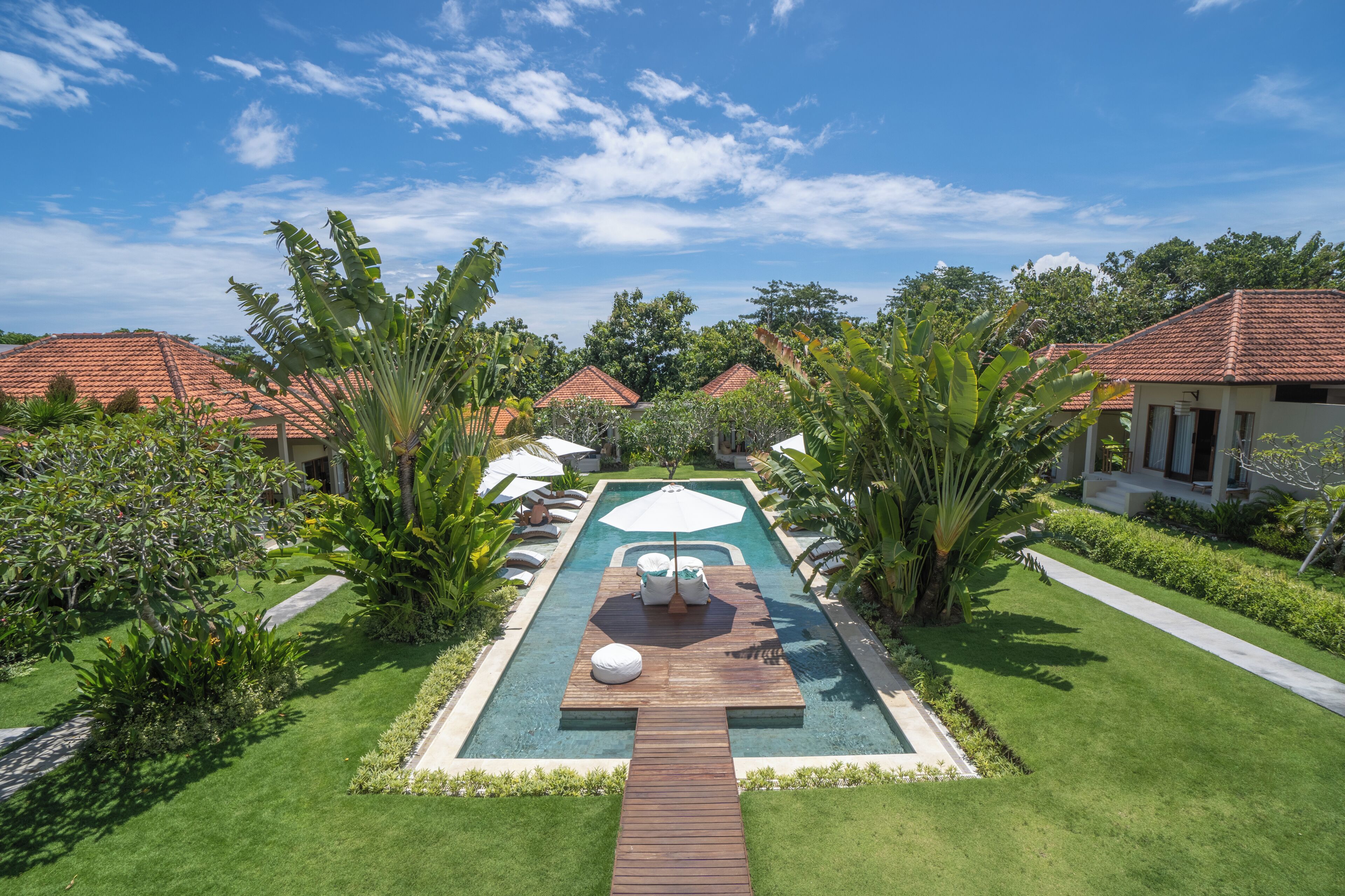 A resort with a swimming pool, wooden deck, and lush greenery.