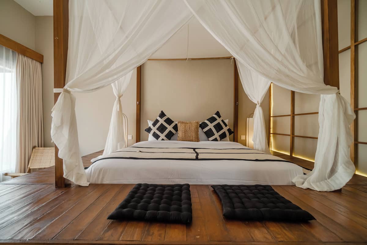 A bedroom with a canopy bed, wooden floor, and a view of the outside through a window.