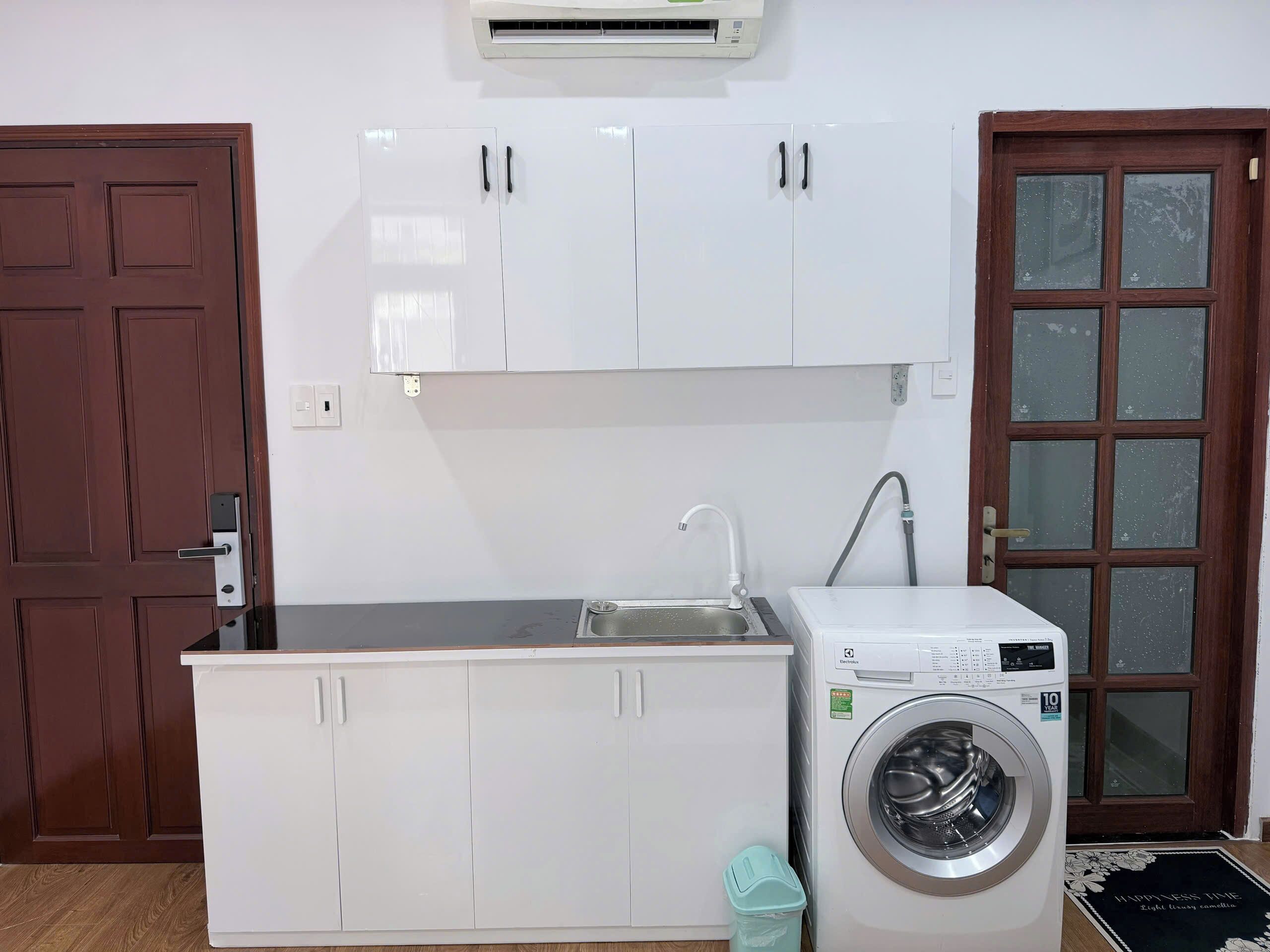 A compact kitchen with white cabinets, a built-in washing machine, a sink, and a door with frosted glass panels.