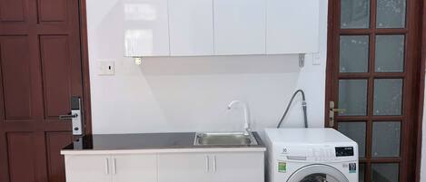 A compact kitchen with white cabinets, a built-in washing machine, a sink, and a door with frosted glass panels.