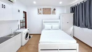 Un dormitori modern i ben il·luminat amb un llit, un armari, una rentadora i un petit cuinetilla.