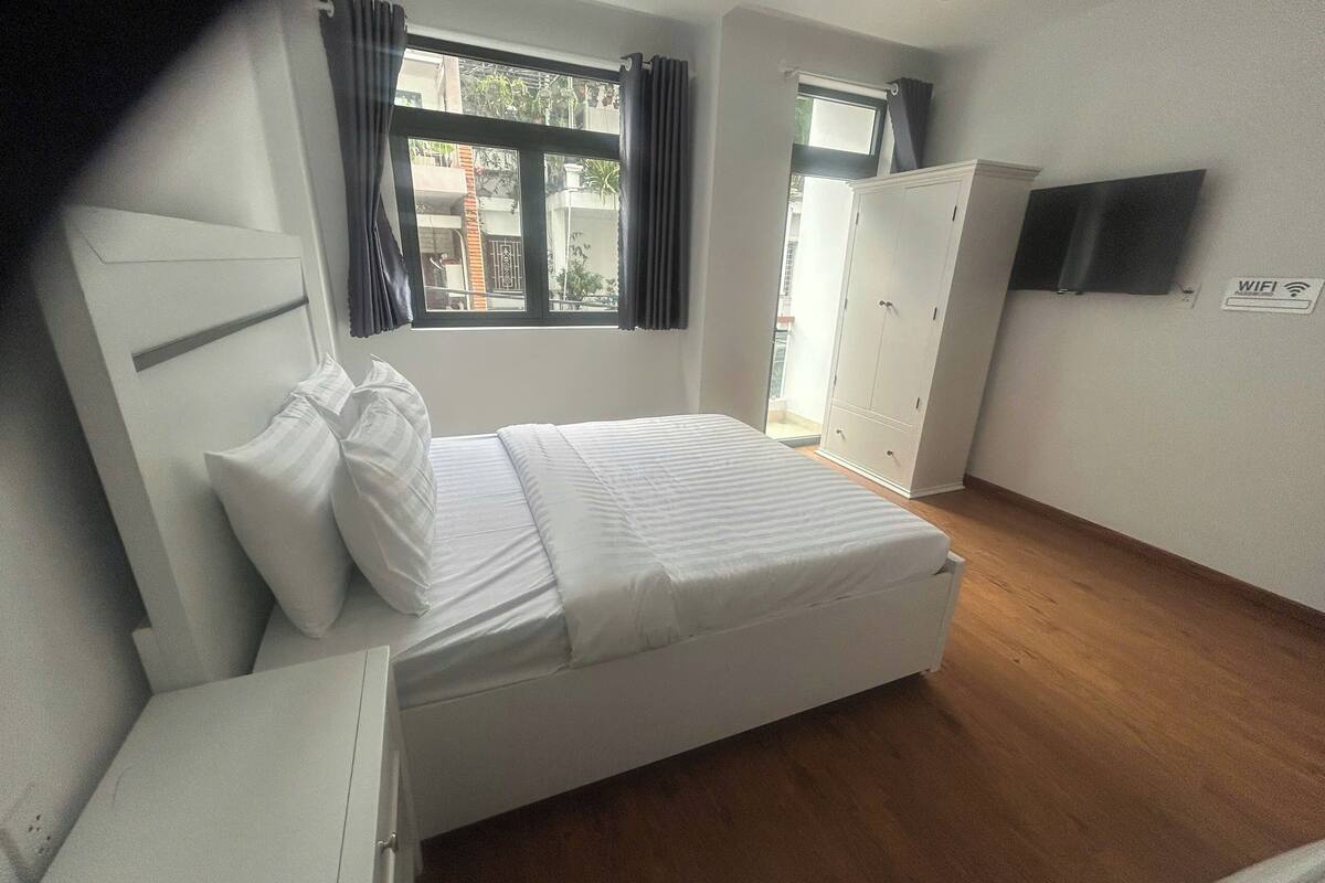 Een slaapkamer met een bed, een kledingkast, een televisie en een raam met gordijnen.