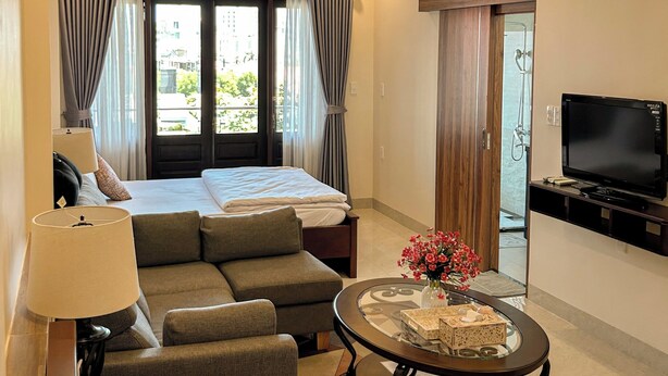 A hotel room with a bed, sofa, TV, and a table with a vase. - Gio Hotel in Hue (Hue)