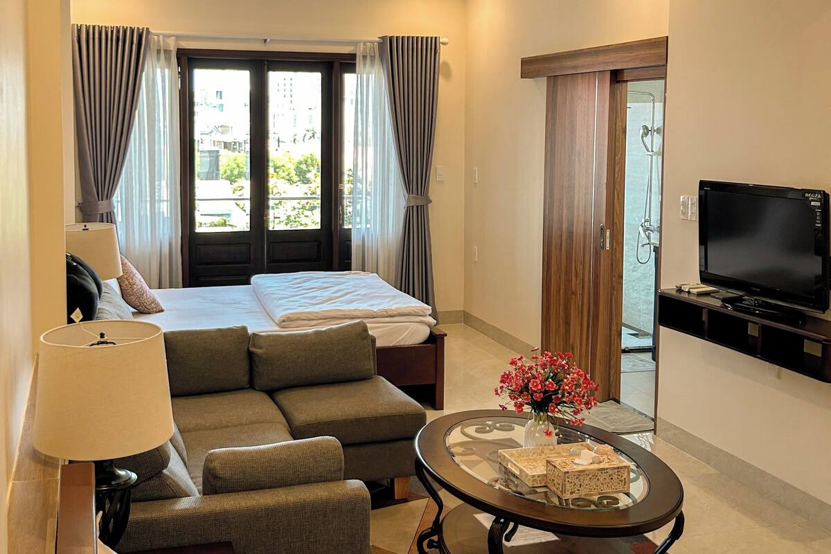 A hotel room with a bed, sofa, TV, and a table with a vase.