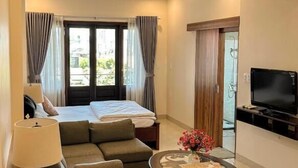 A hotel room with a bed, a sofa, a small table with flowers, a TV, and a ceiling fan. - Gio Hotel in Hue (Hue)