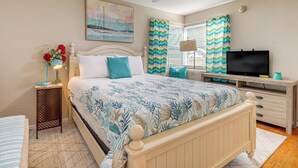 Un dormitorio con cama, televisor, escritorio y ventana con cortinas.