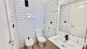 A bathroom with white subway tiles, a toilet, a bidet, and a sink with a mirror.