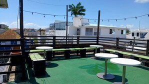 Un patio exterior con piso verde, mesas redondas blancas y bancos verdes.