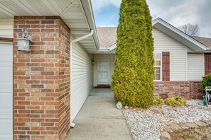 A residential house with a brick exterior, a front door, and a tall coniferous tree in the front yard.