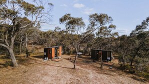 Dos cabañas pequeñas y modernas en un entorno natural con vegetación escasa y cielo despejado.