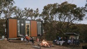 Una cabaña moderna y compacta con un amplio ventanal corredera, un pequeño espacio de estar al aire libre y un pozo de fuego.