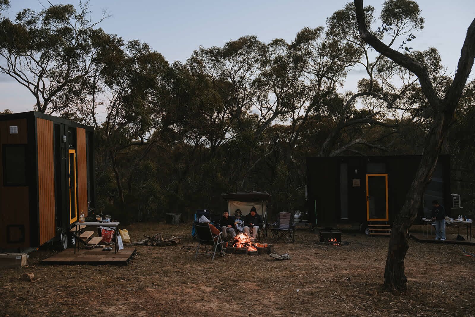 Un camping con una fogata, tiendas de campaña y un pequeño edificio con una puerta.